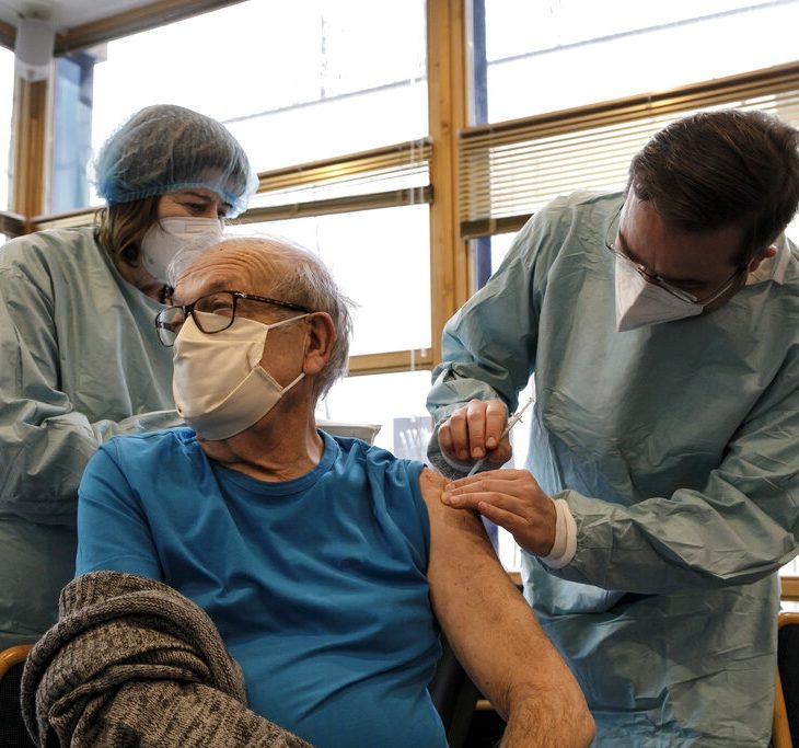 Two medical professionals administering vaccine to man in mask
