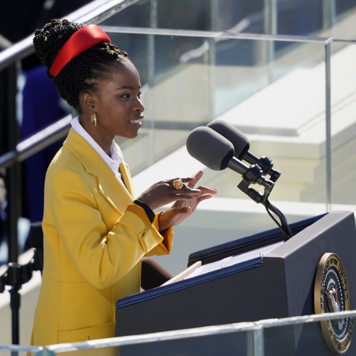 Amanda at podium in yellow coat and red headband
