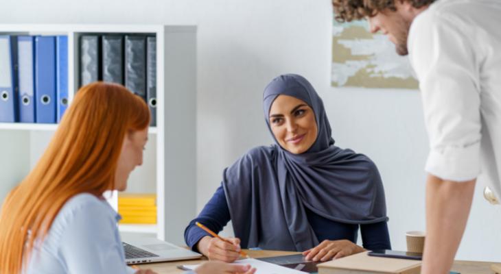 Woman in head scarf facing camera working with two coworkers