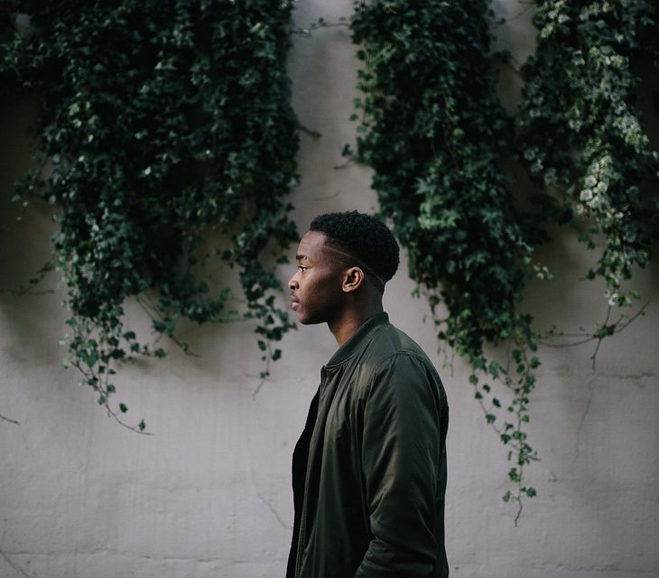 Black man in profile stands in front of greenery wall