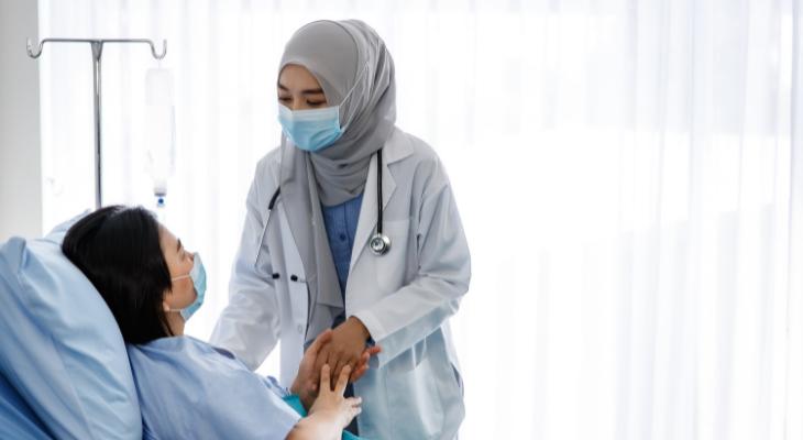 Doctor in headscarf assists patient in hospital bed