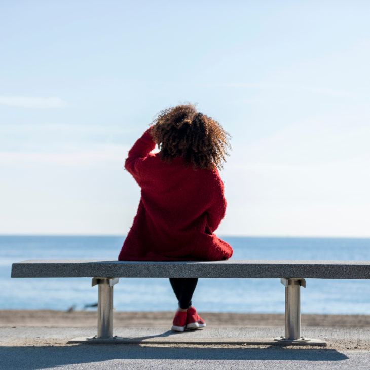 Woman sitting on bench overlooking ocean