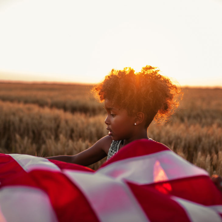 Girl with curly hair in field with American flag