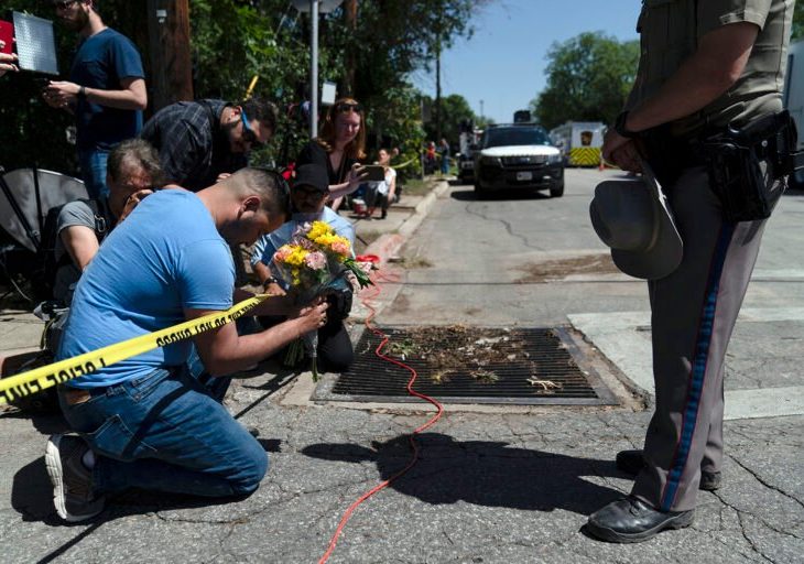 People pray on knees and hold flowers n side of police tape