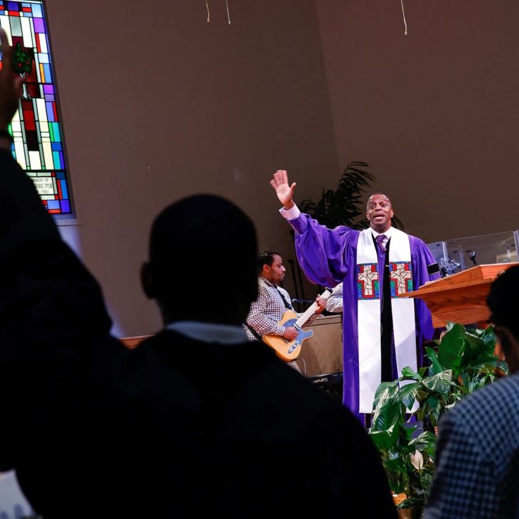 Pastor in robes with raised hand in front of church sanctuary