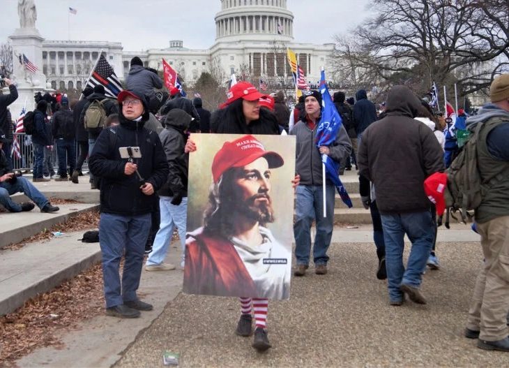 protester in crowd holding picture of Jesus with MAGA hat on