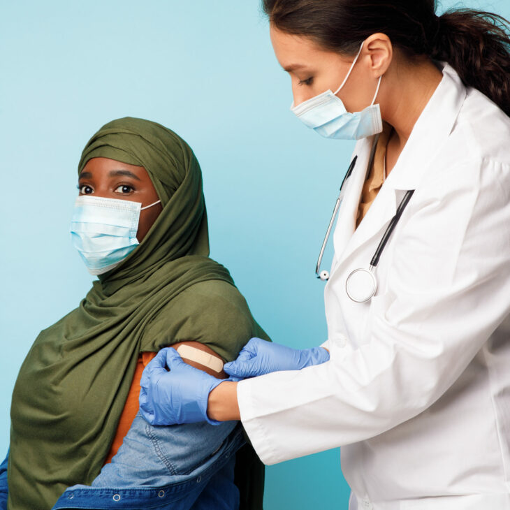 Doctor Making Vaccine Injection To African Muslim Lady, Blue Background