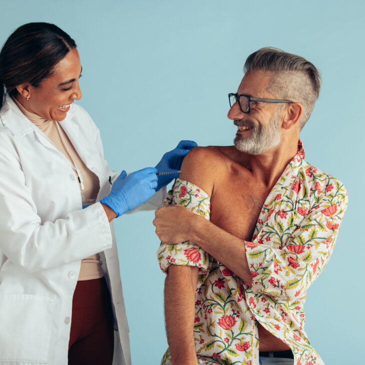 Smiling man getting flu shot from a female doctor. Female healthcare professional giving vaccine to mid adult man.