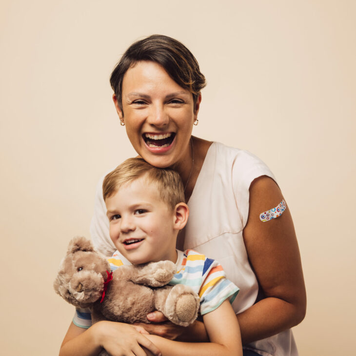 Cheerful mother and son after vaccination on brown background. Woman holding her son with a teddy bear.