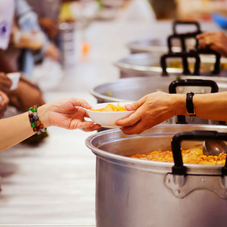 line of soup pots with hands reaching over to give plate to person on the left