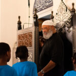 Sharif Salim of the Diyanet Center of America gives a tour of the mosque to students in the Vacation Interfaith School of Bowie, Maryland. He's standing by the kursi, a chair used by Islamic scholars to give lectures on religion. (© Shelby Swann Photography)