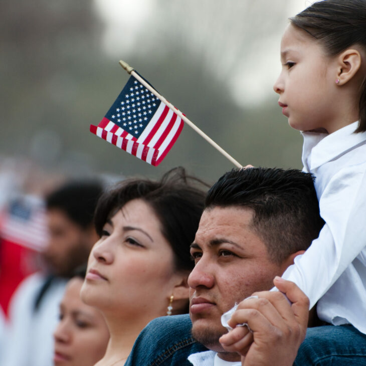 young girl on shoulders of father, in profile, holding a flag