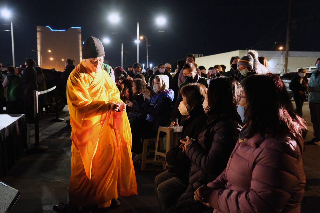 The Venerable Guo Yuan, in orange, speaks to attendees at a Buddhist prayer ceremony on Tuesday, Jan. 31, 2023, outside Star Ballroom Dance Studio in Monterey Park, California. RNS photo by Alejandra Molina
