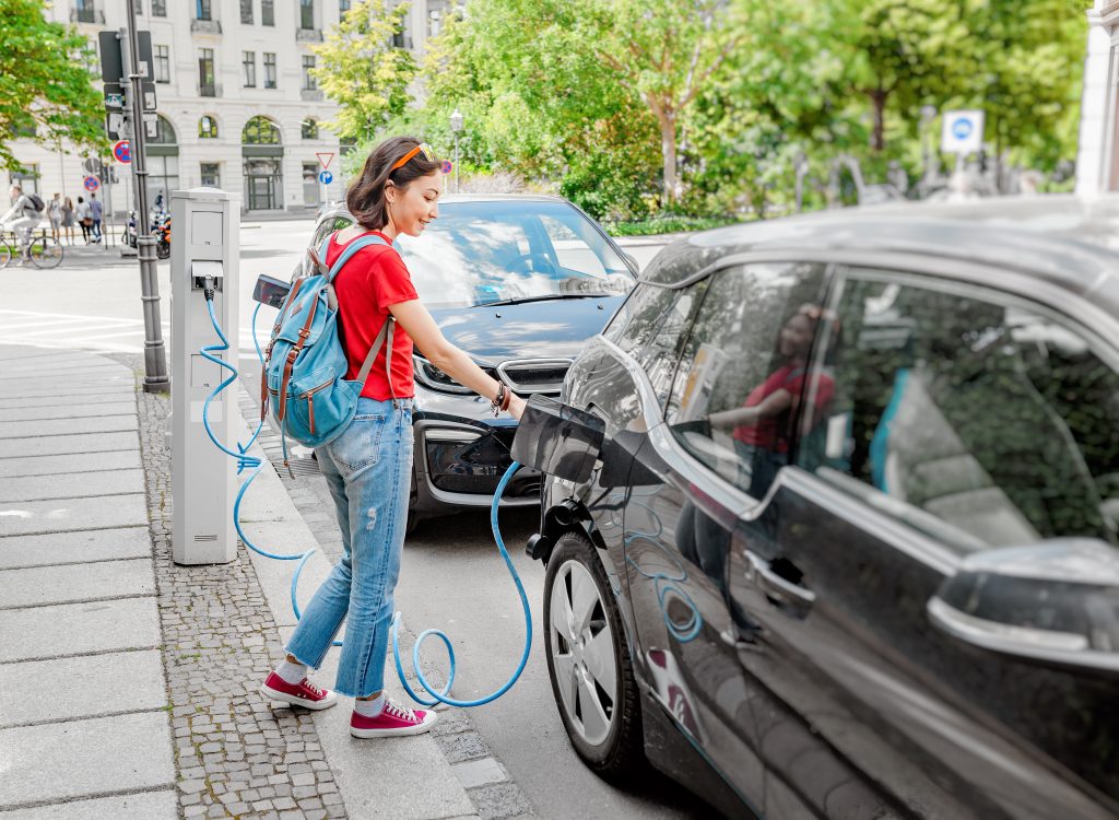 Woman charging her electronic car at special parking, alternative energy. (frantic00/Shutterstock)