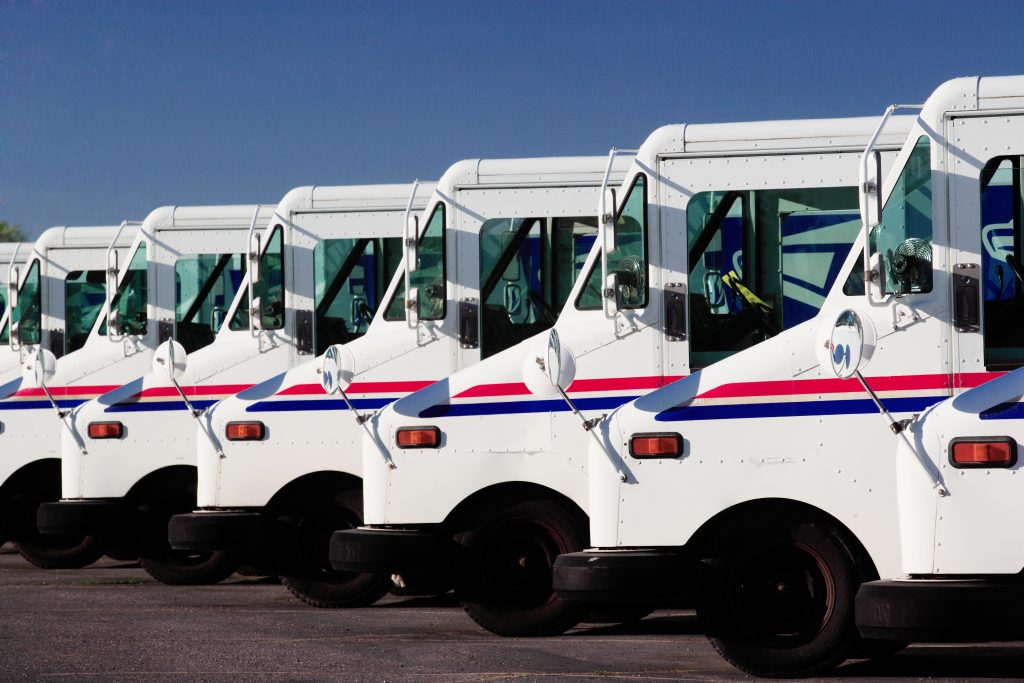 A row of US Postal service trucks, parked waiting to deliver the mail. (B Brown/Shutterstock)
