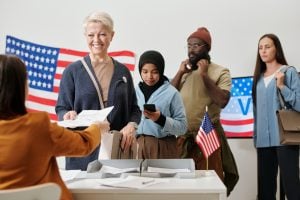 Queue of voters standing by desk of poll workers on election day. (shironosov/iStock/Getty Images Plus)