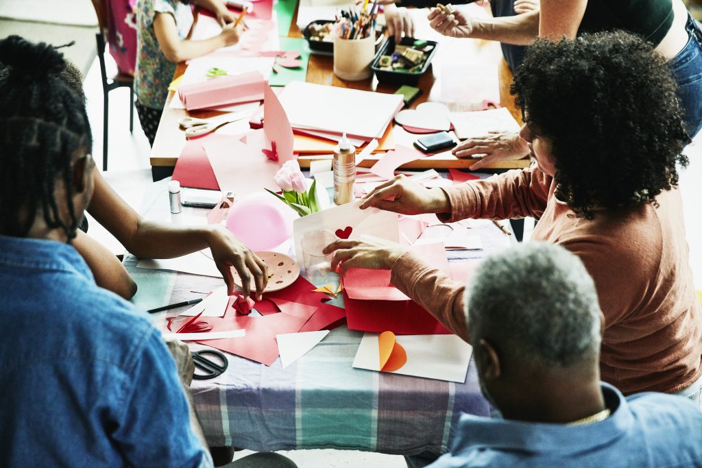 Family and friends gathered around table in home making Valentine's Day cards. (Thomas Barwick/Getty Images)
