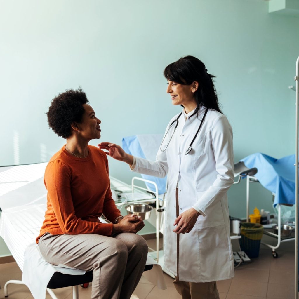 Woman is dressed casually and smiling at the doctor as she listens attentively.