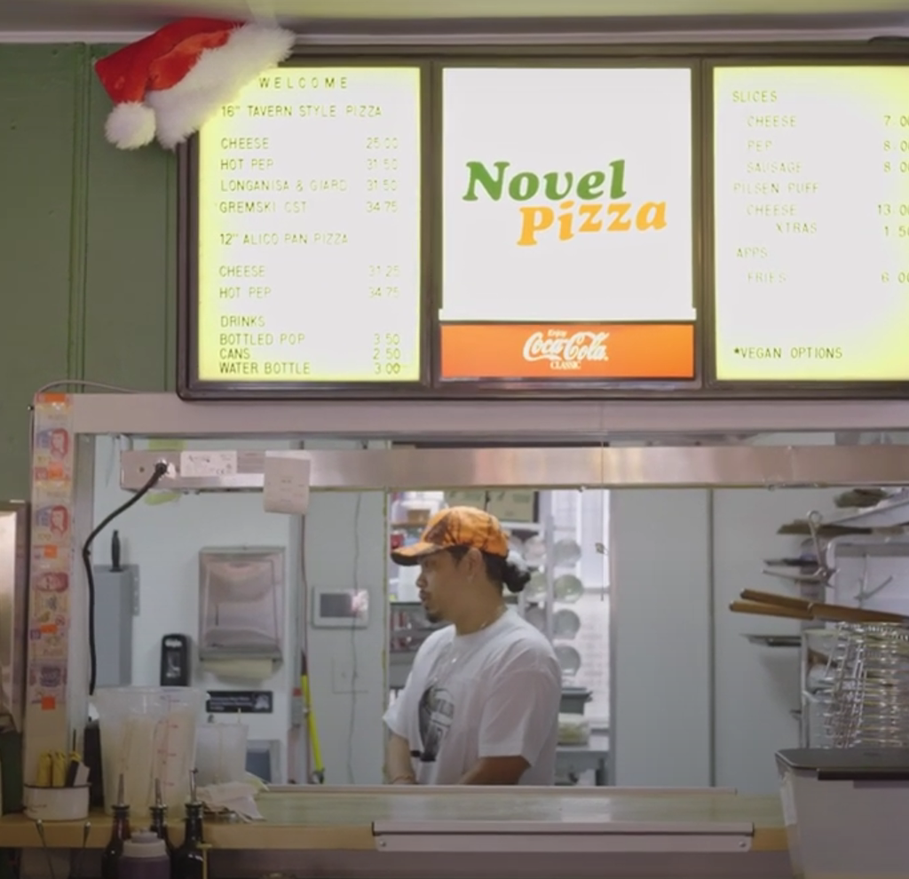 The menu on the wall hangs over a window to order that looks into the kitchen at Novel Pizza.