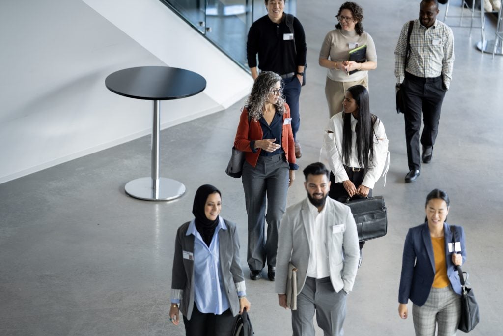 A small group of diverse business professionals walk in a large corporate office building. (Getty Images/ FatCamera)