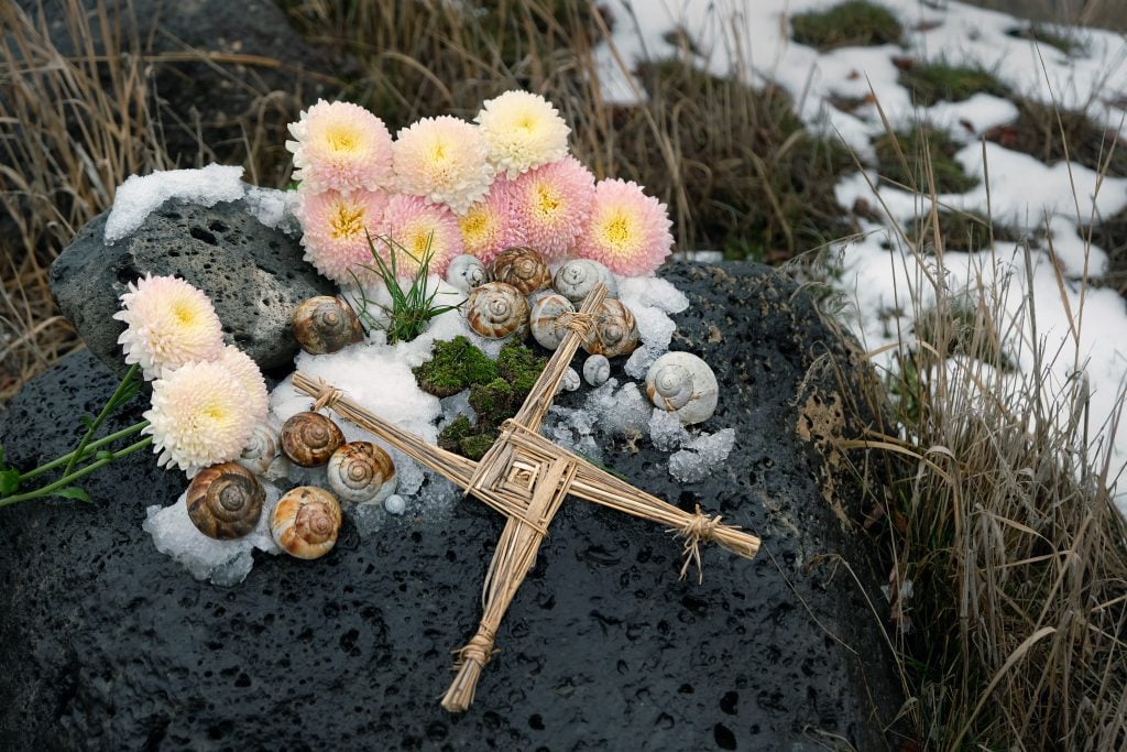 Wiccan altar for Imbolc holiday. Brigid's cross of straw, candles and snail shells on big stone outdoor, abstract nature background. symbol of Imbolc, spring equinox. witchcraft, pagan magic ritual (Shutterstock) 