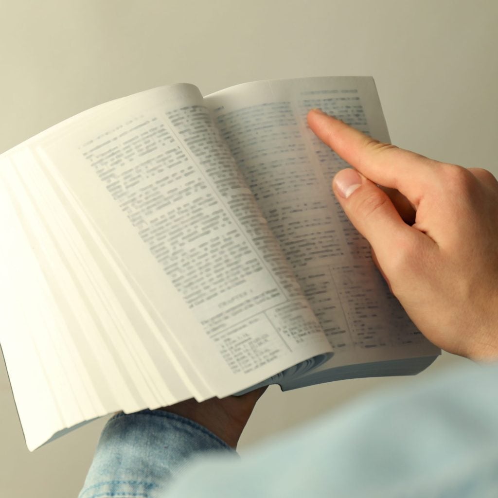 Man reading Holy Bible in English language on light background, closeup
