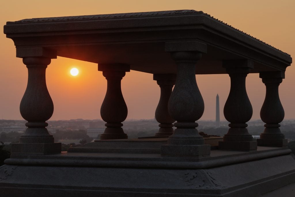 ARLINGTON, VIRGINIA - JUNE 11: The sunrise and the Washington Monument are seen through the grave of architect, engineer and city planner Pierre Charles L'Enfant at the top of Arlington National Cemetery on June 11, 2025 in Arlington, Virginia. L'Enfant served as an officer in the Continental Army Corps of Engineers during the American Revolution and is most famous for designing the plan for Washington, DC. The nation's capital is preparing for weekend events celebrating the 250th anniversary of the founding of the U.S. Army. (Photo by Chip Somodevilla/Getty Images)