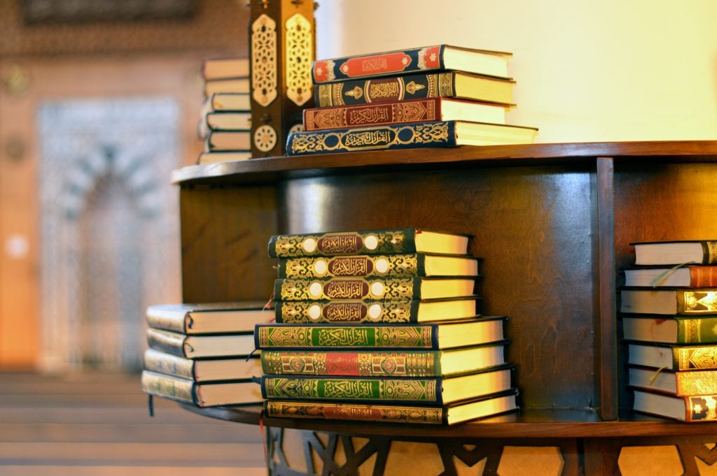 Holy Quran books in a row standing on a wooden shelf inside a mosque, English translation of the Arabic Text (The Holy Noble Quran), it's the central religious text of Islam, revelation from God Allah, selective focus