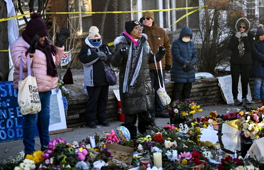 MINNEAPOLIS, MINNESOTA - JANUARY 14: June Pierce (C) prays during a vigil at a memorial near the site where Renee Good was killed a week ago on January 14, 2026 in Minneapolis, Minnesota. Good was fatally shot by an immigration enforcement agent during an incident in south Minneapolis on January 7. (Photo by Stephen Maturen/Getty Images)
