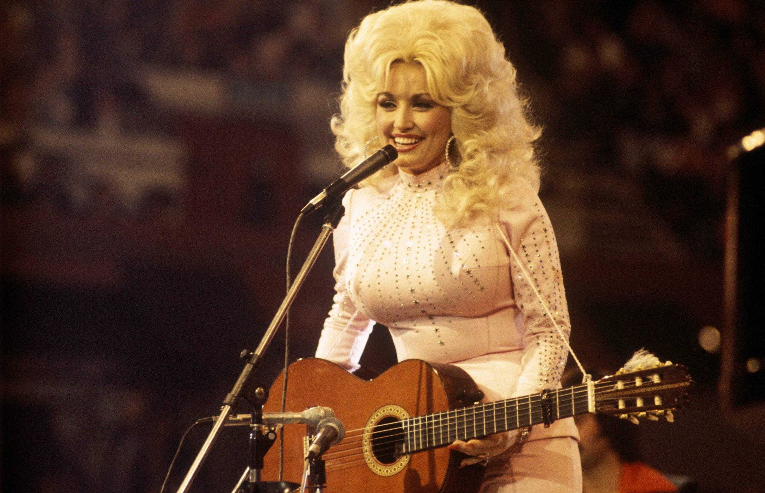 Dolly Parton performs with a guitar, 1976. (Photo by David Redfern/Redferns, Getty Images)