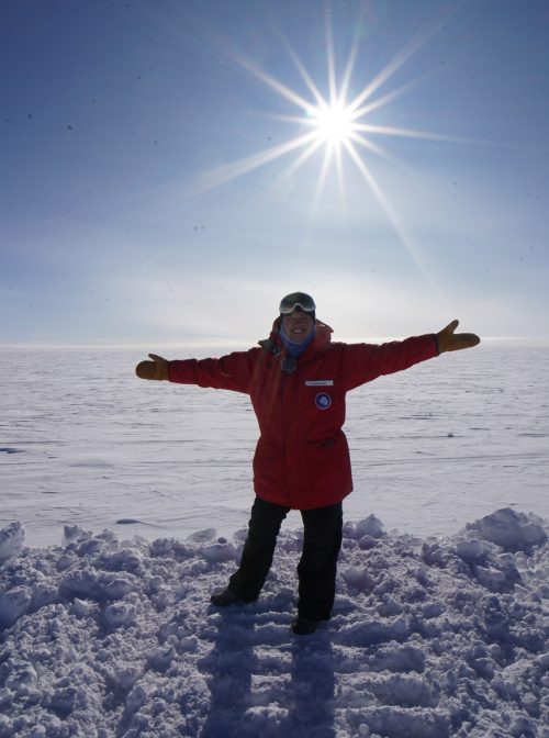 Elaine in red winter jacket with outstretched arms in the center of a snowy tundra.