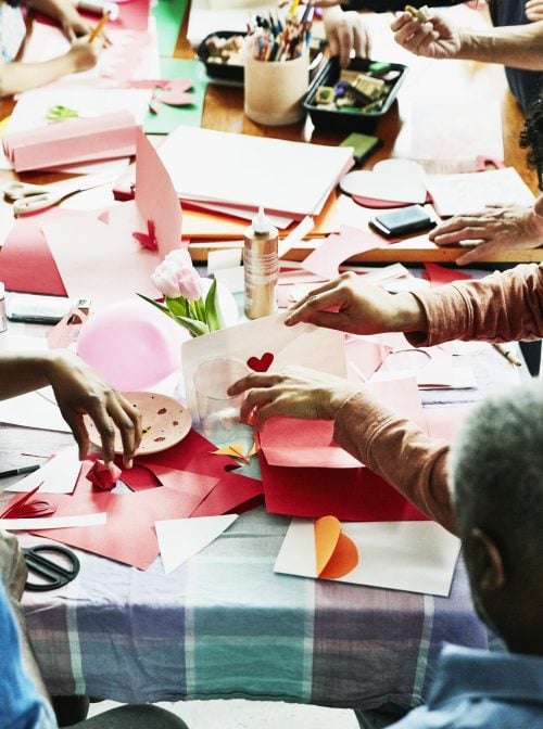 Family and friends gathered around table in home making Valentine's Day cards. (Thomas Barwick/Getty Images)
