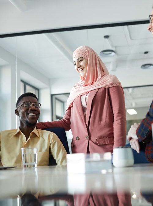 Business team standing by meeting table in conference room, focus on Muslim woman wearing headscarf standing by African-American colleague