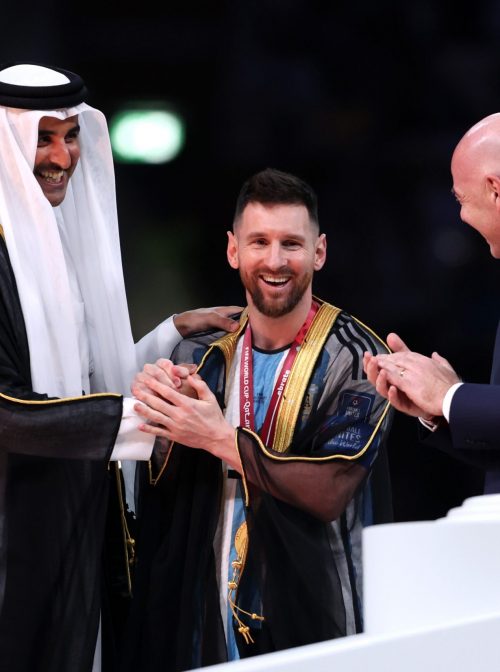 LUSAIL CITY, QATAR - DECEMBER 18: Lionel Messi of Argentina is presented with a traditional robe by Sheikh Tamim bin Hamad Al Thani, Emir of Qatar, while Gianni Infantino, President of FIFA, looks on during the awards ceremony after the FIFA World Cup Qatar 2022 Final match between Argentina and France at Lusail Stadium on December 18, 2022 in Lusail City, Qatar. (Photo by Clive Brunskill/Getty Images)