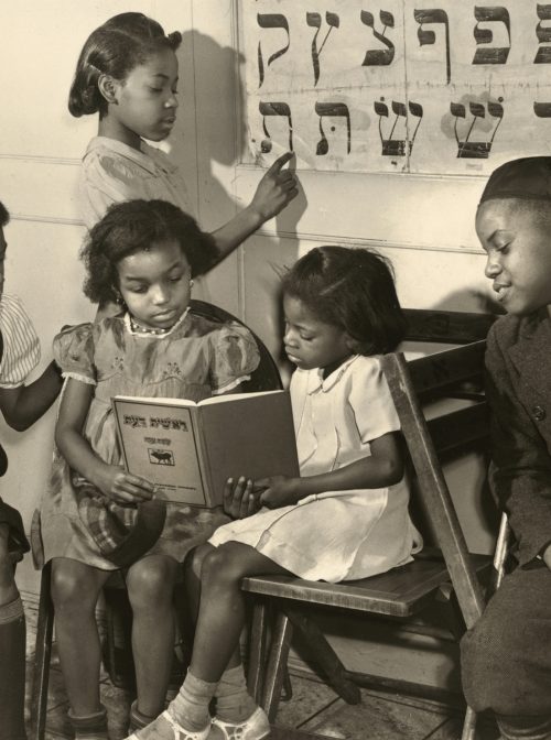 Young Black children read out of a book written in Hebrew in 1940 in Harlem, New York. Another girl studies a Hebrew alphabet. From the series: The Commandment Keepers: African American Jewish Congregation in Harlem. (Collection of the Smithsonian National Museum of African American History and Culture, © Alexander Alland Jr.)