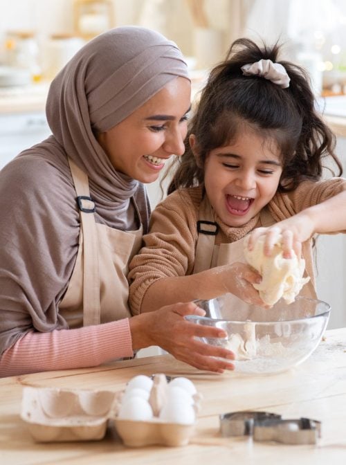 Cheerful Muslim Mom In Hijab And Her Little Daughter Having Fun At Home, Baking Pastry In Kitchen Together, Kneading Dough While Preparing Cookies, Enjoying Cooking Homemade Food. Closeup Shot